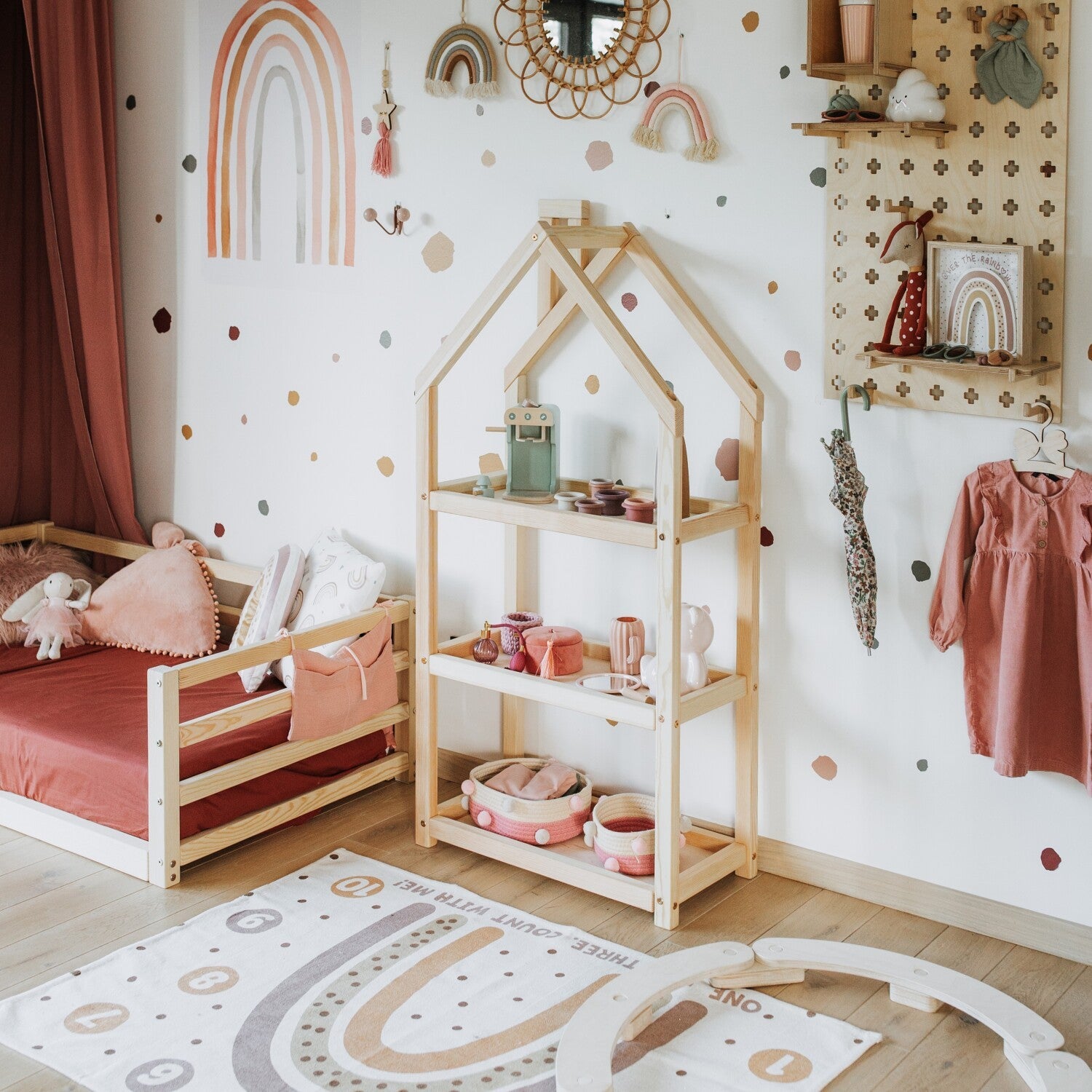 Natural birch house shelf beside bed with toys, books, and storage in warm bedroom