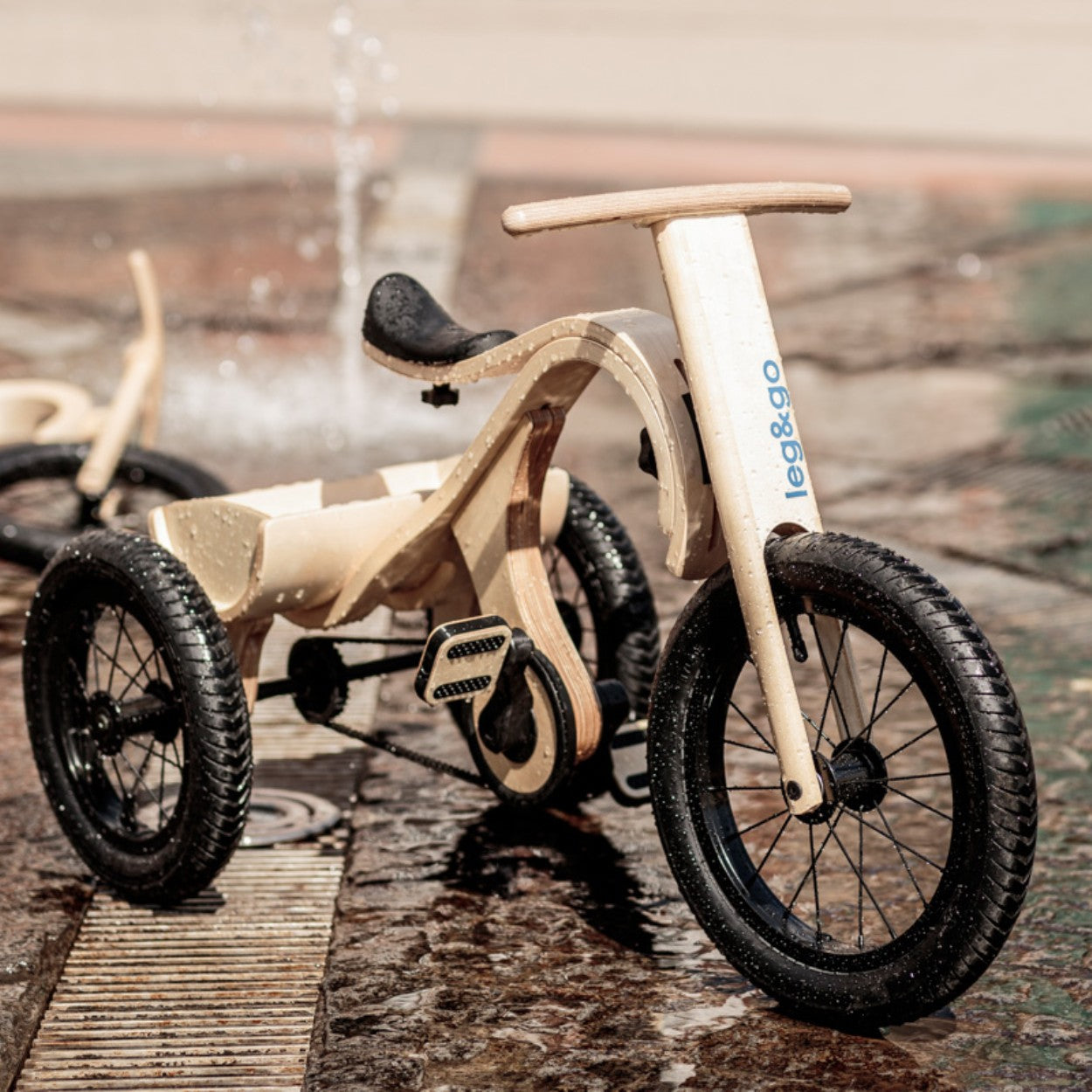Side view of wooden tricycle add-on showing three black wheels and handlebar
