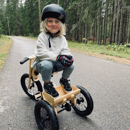 Girl with helmet riding leg&go tricycle add-on on forest path