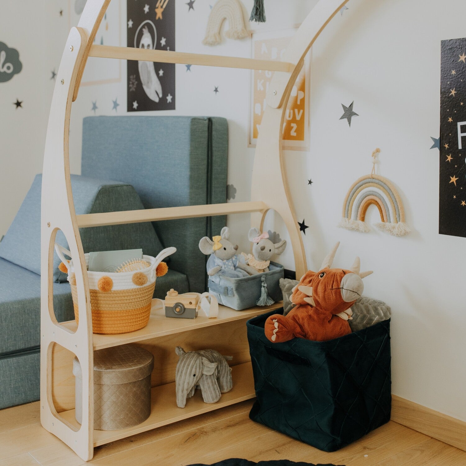 Wooden play stand filled with storage baskets and toys next to blue upholstered chair