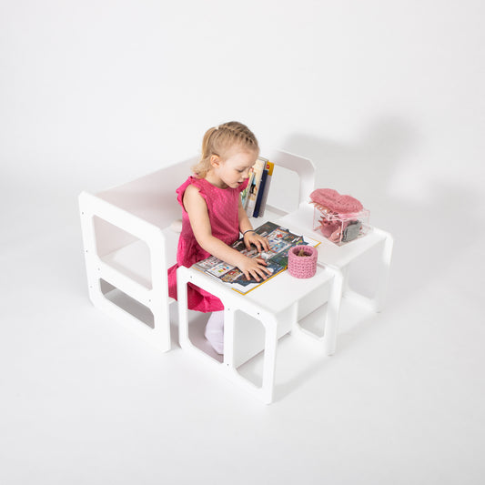 Toddler in pink dress sitting at white Montessori weaning table with matching chair, playing with toys