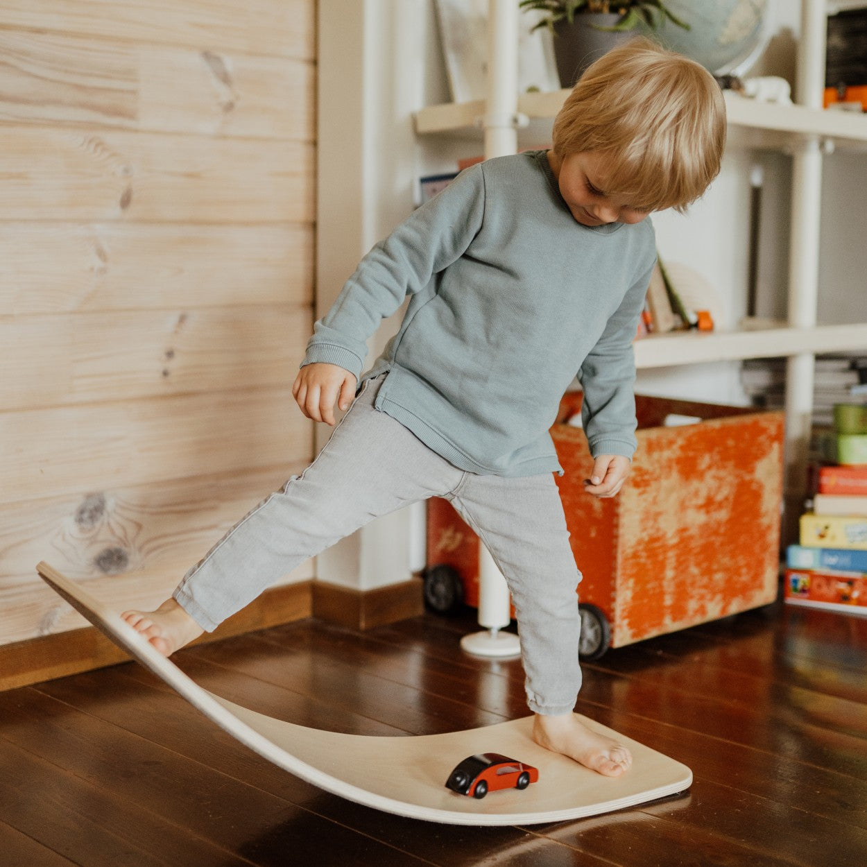 Child standing on wooden balance board with one foot, practicing balance and coordination