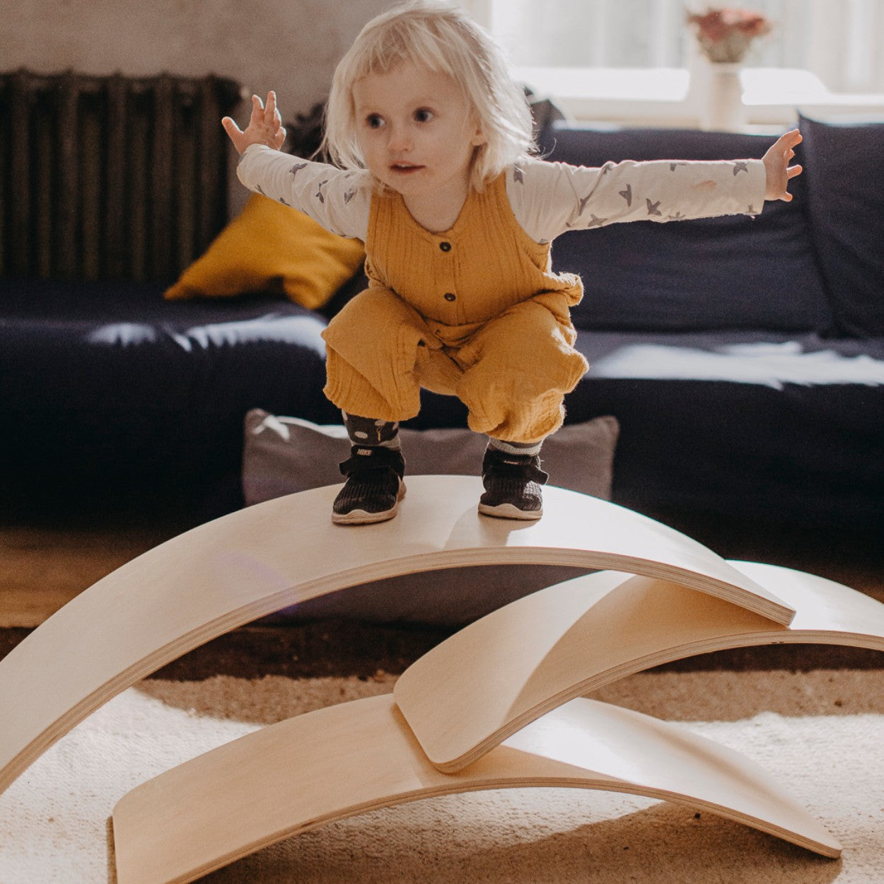 Child playing on stacked wooden balance boards configured as tunnel and bridge structure