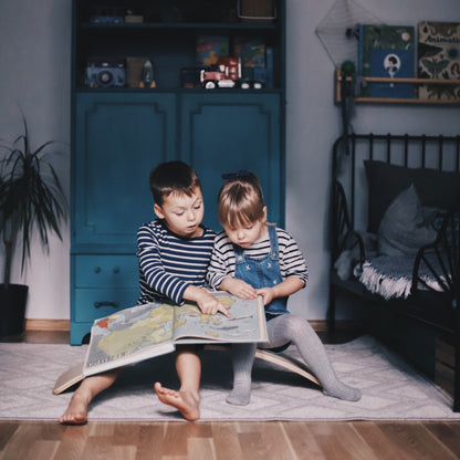 Two toddlers sitting on curved balance board reading a picture book together
