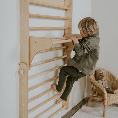 Toddler climbing Swedish wall mounted on white wall near wicker furniture