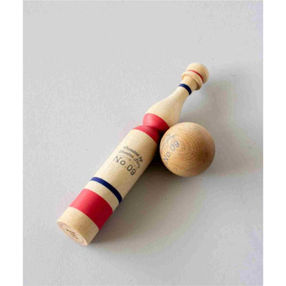 Close-up of single wooden bowling pin with red bands next to one wooden ball on white background