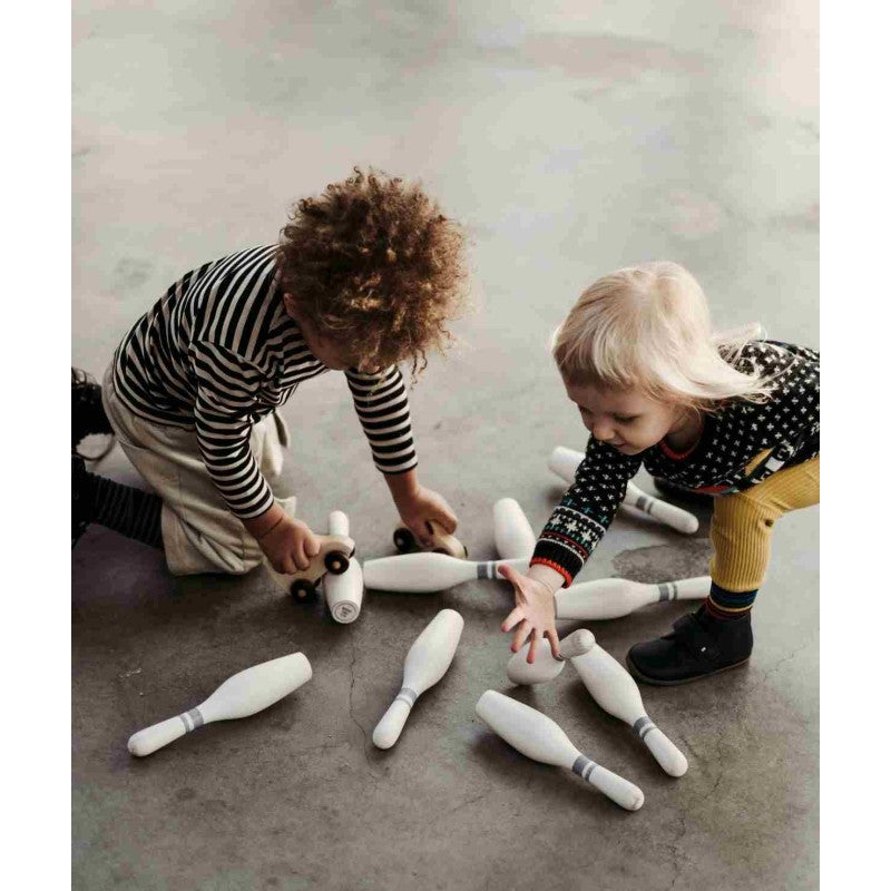 Two toddlers playing together with wooden bowling pins on concrete floor
