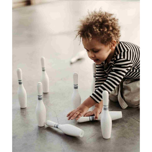 Toddler in striped shirt playing with wooden bowling pins on floor