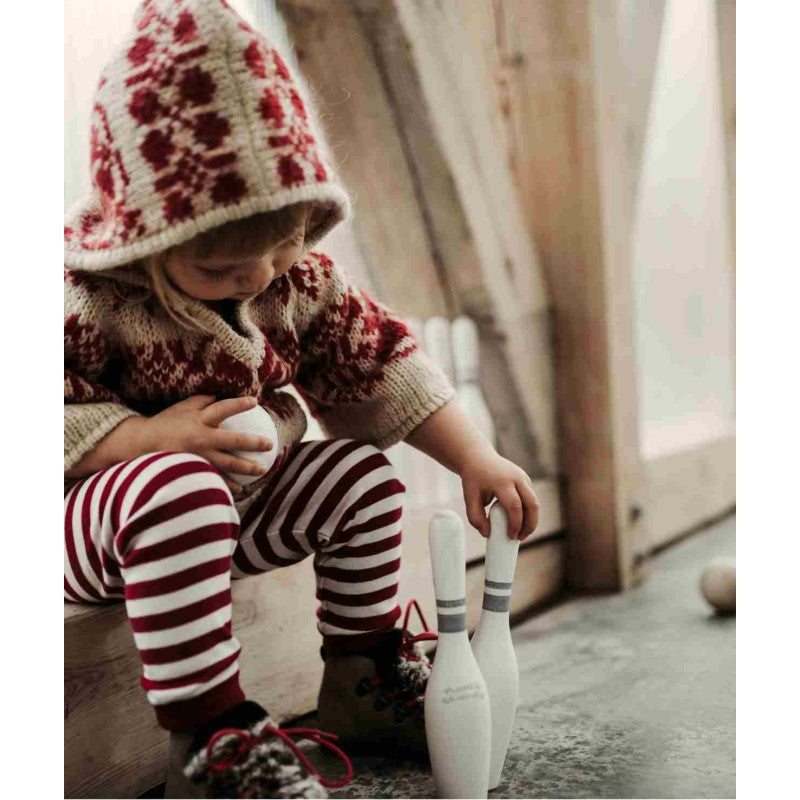 Child in cozy sweater setting up wooden bowling pins for play