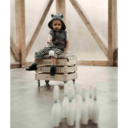 Doll sitting on wooden crate with bowling pins arranged in distance