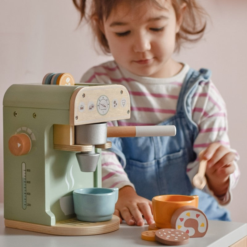 Toddler playing with wooden coffee maker, pouring from portafilter into blue cup during pretend barista play