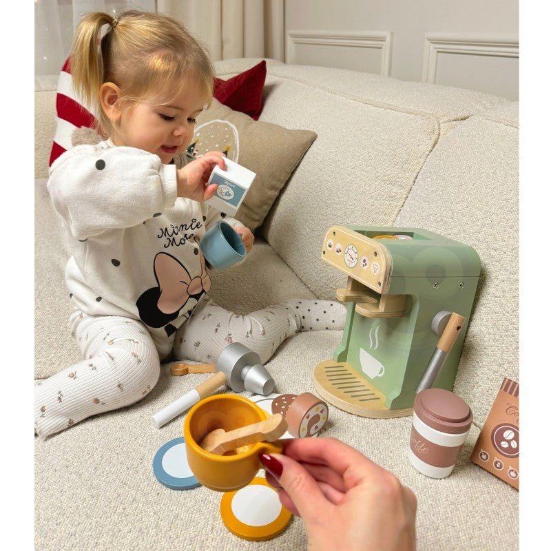 Toddler sitting on couch using wooden coffee maker, holding milk carton accessory during imaginative play