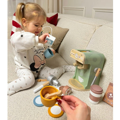 Toddler sitting on couch using wooden coffee maker, holding milk carton accessory during imaginative play