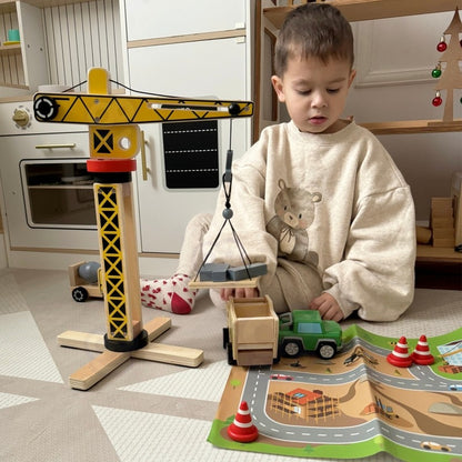 Toddler playing with wooden construction set including crane, vehicles and traffic cones on activity mat