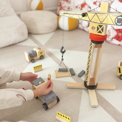 Child's hand holding wooden construction truck near crane during hands-on motor skill play