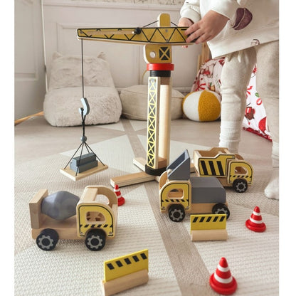 Child operating wooden construction crane and vehicles on bedroom carpet with play accessories