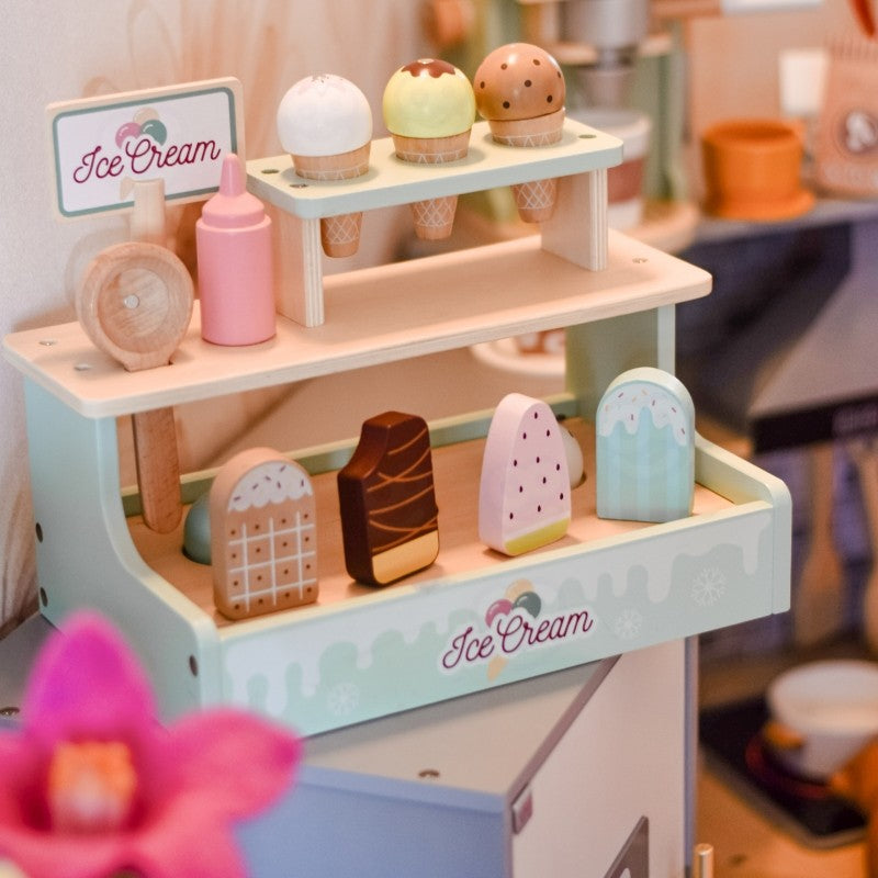 Wooden ice cream shop set on desk with blurred home interior and plant in background