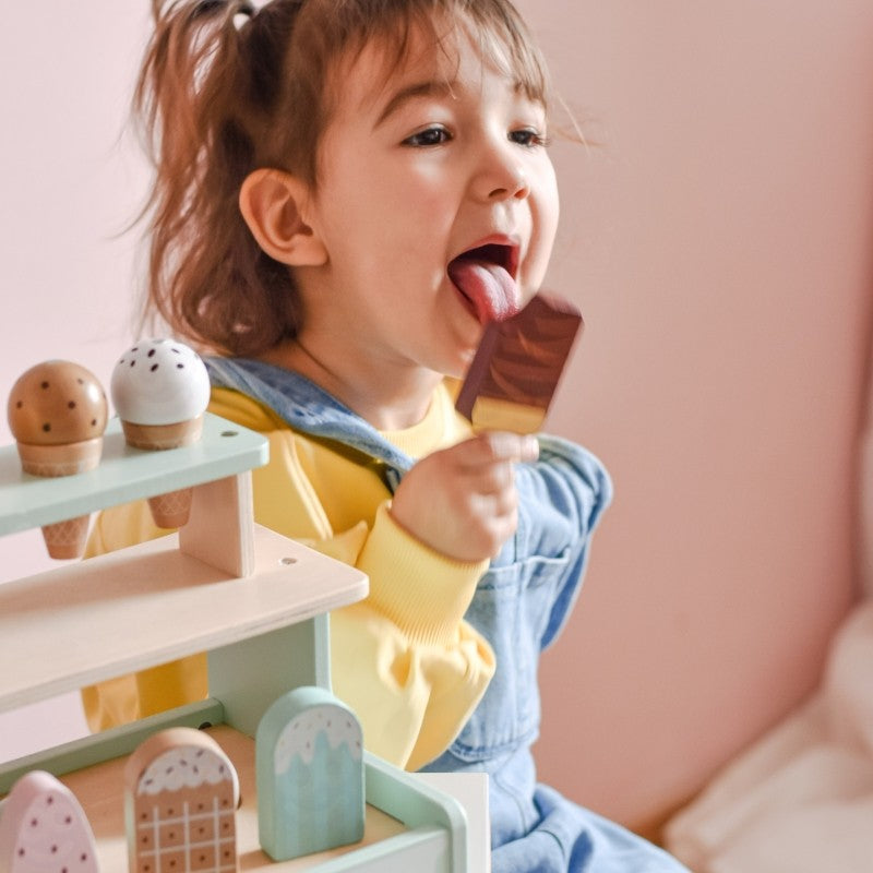 Toddler eating wooden popsicle while playing with ice cream shop set