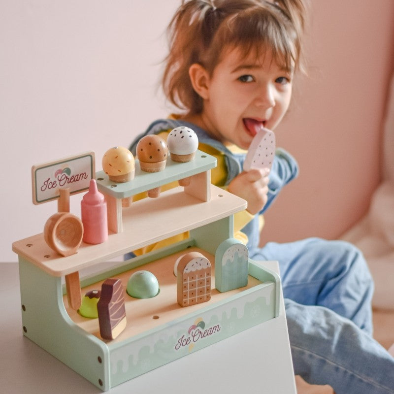 Young child pretending to serve ice cream with scoops from wooden shop stand