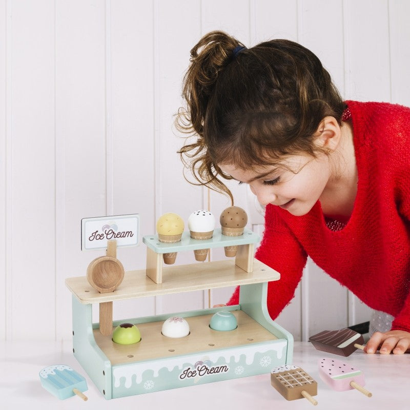 Child leaning toward wooden ice cream shop set to play with magnetic scoops and accessories
