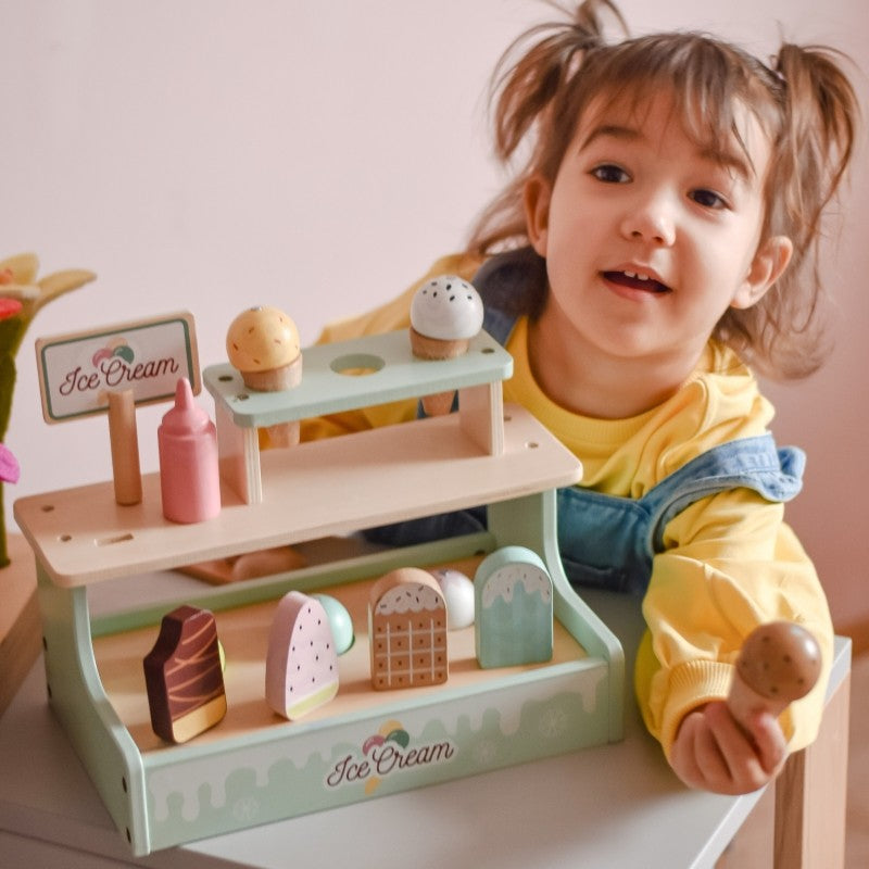 Smiling child holding wooden ice cream shop set with playful expression