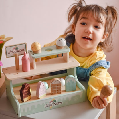 Smiling child holding wooden ice cream shop set with playful expression