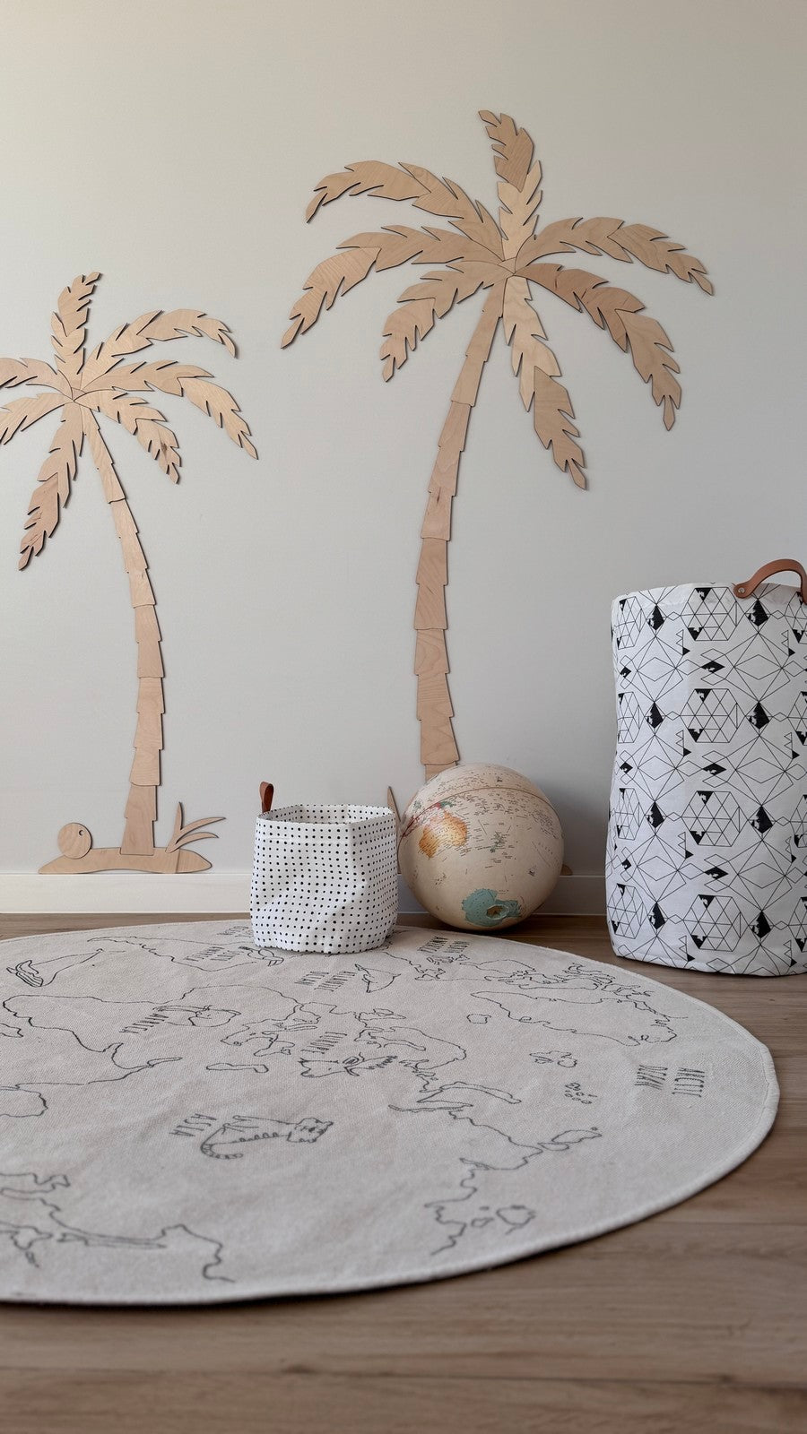 Two hand-cut wooden palm trees in natural plywood displayed on a nursery floor with toys