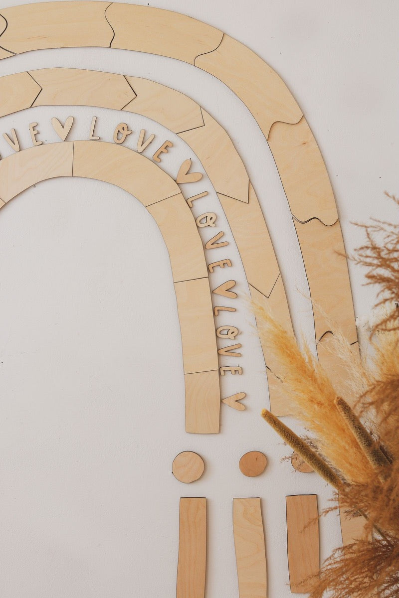 Close-up of rainbow wall art showing engraved love message on curved plywood pieces and wooden pegs