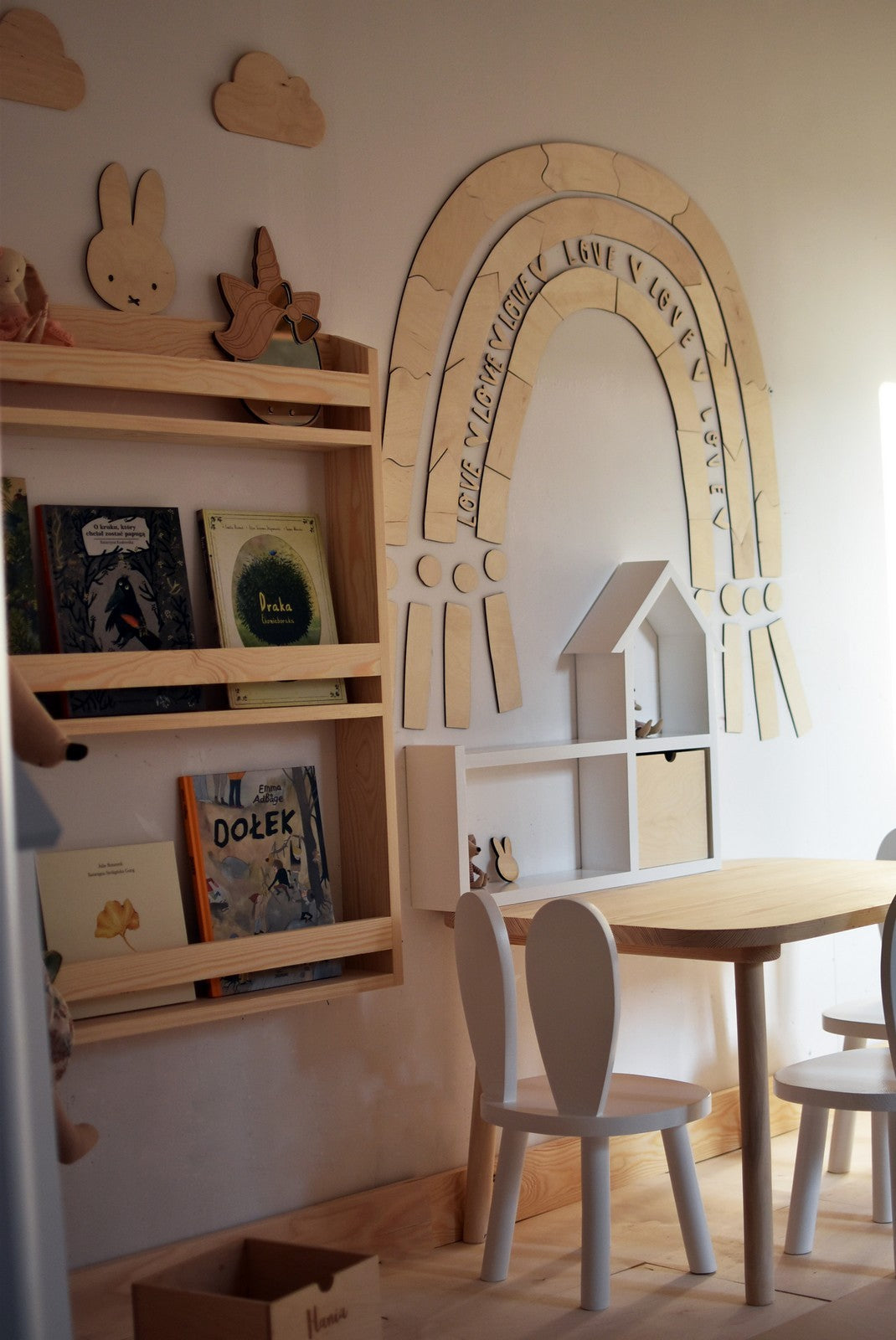 Rainbow puzzle wall decoration mounted in child's playroom above wooden shelf and table with decor