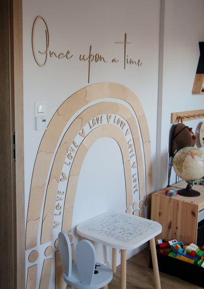 Rainbow wood wall decoration installed in bedroom above white table and chair with nursery styling