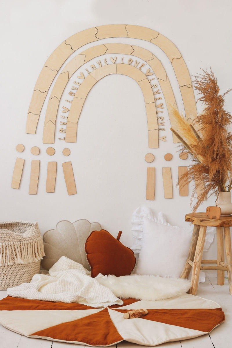 Birch plywood rainbow puzzle wall art mounted above cozy reading nook with cushions and blanket