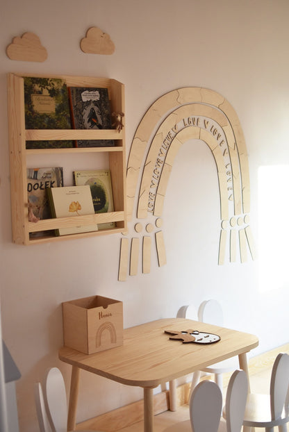 Rainbow wall decoration hanging in playroom next to wooden shelf unit and dining table setup