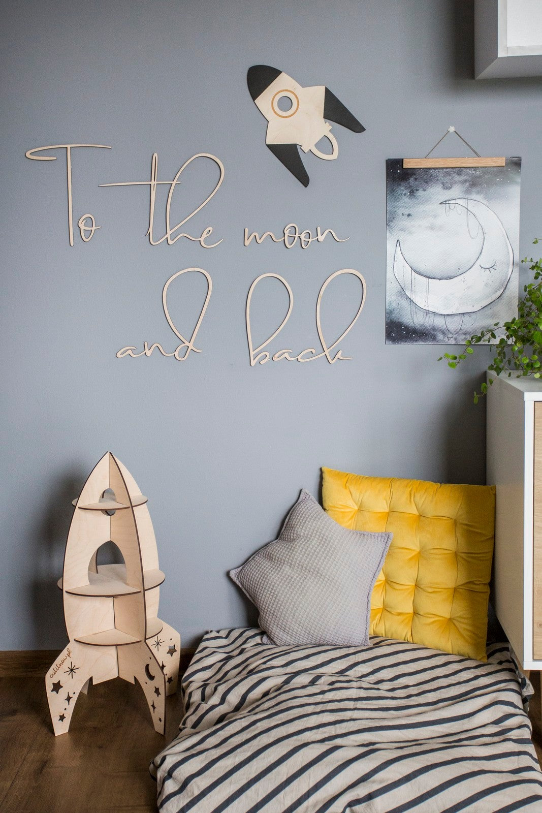 Close-up of To the Moon and Back plywood sign showing handcrafted lettering and rocket design